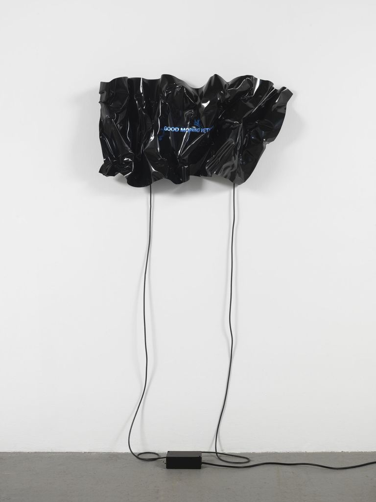 Crumpled black vinyl sheet with blue neon text reading "GOOD MORNING VIETNAM" suspended on white wall.