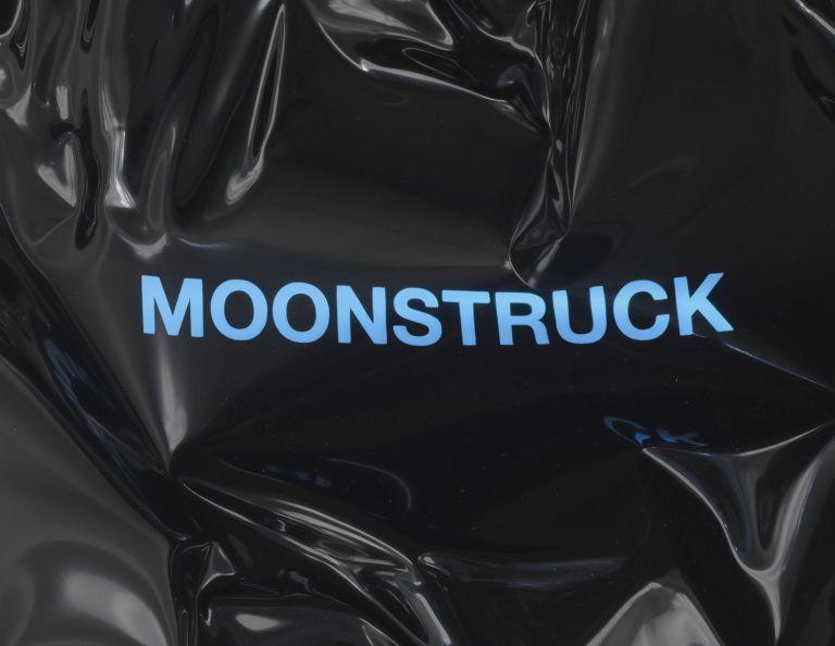 Black heat-folded vinyl sheet mounted on white wall with blue neon text reading 'MOONSTRUCK'