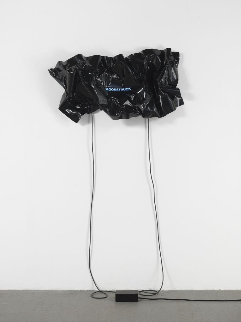 Black heat-folded vinyl sheet mounted on white wall with blue neon text reading 'MOONSTRUCK'