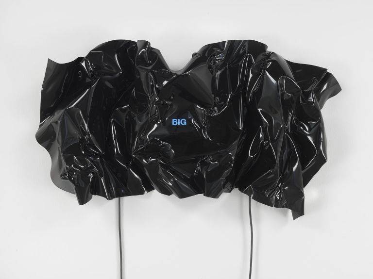 Black heat-folded vinyl sheet on white wall with small blue neon text reading 'BIG'