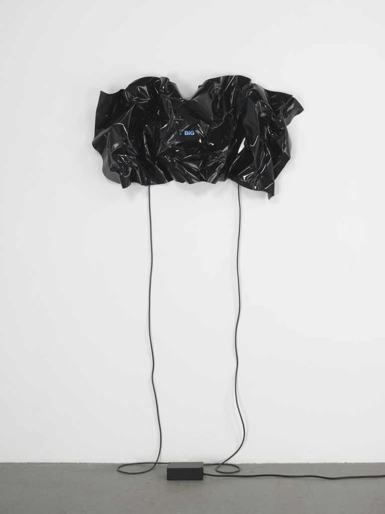 Black heat-folded vinyl sheet on white wall with small blue neon text reading 'BIG'