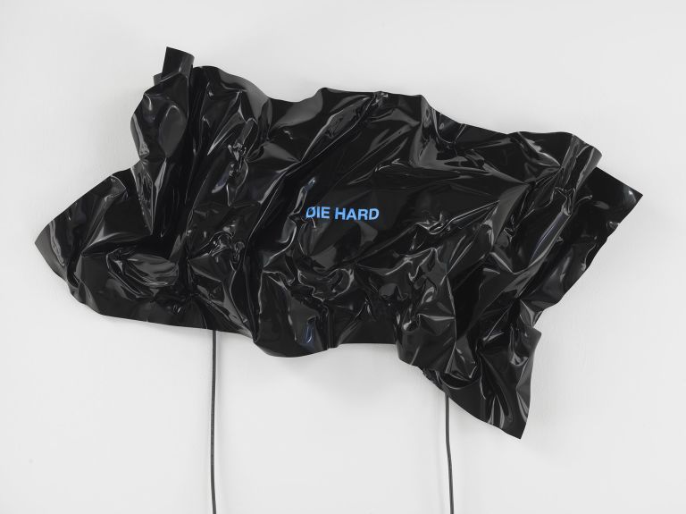 Black heat-folded vinyl sheet mounted on wall with blue neon text reading 'DIE HARD'