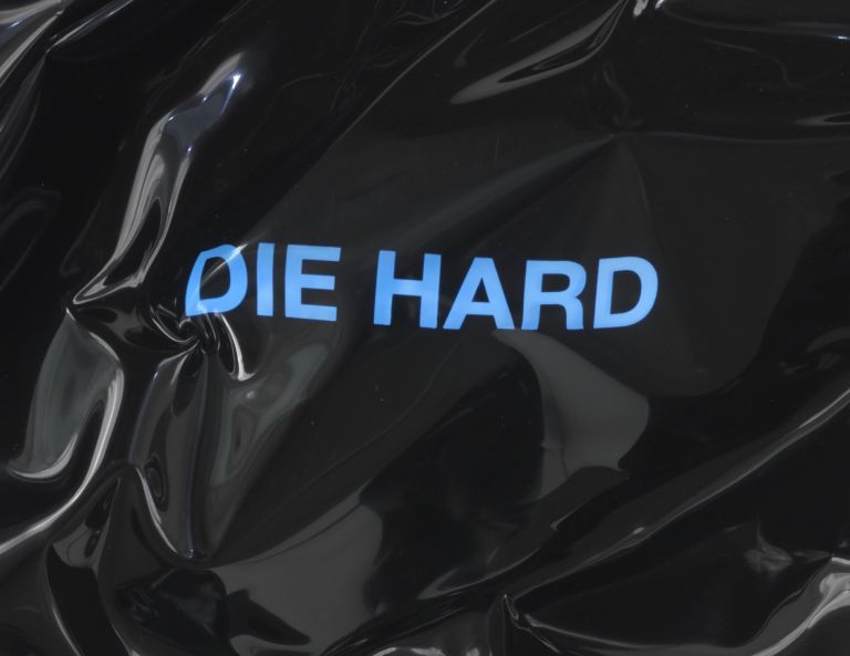 Black heat-folded vinyl sheet mounted on wall with blue neon text reading 'DIE HARD'
