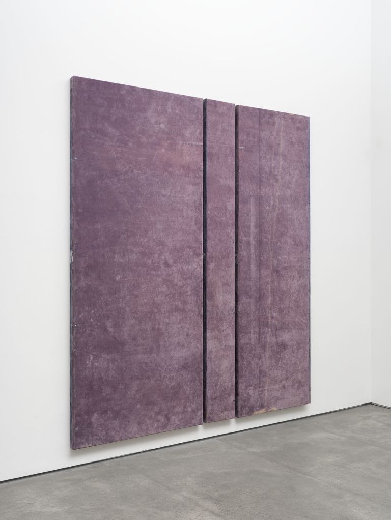Three tall purple-mauve panels with vertical divisions mounted on white gallery wall.