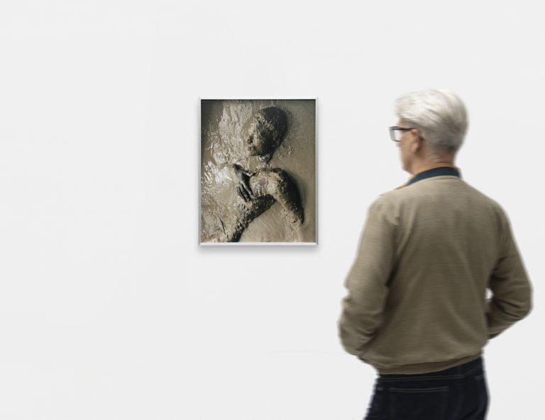 Monochromatic sculptural portrait relief showing profile of figure with textured surface, mounted in gallery frame.