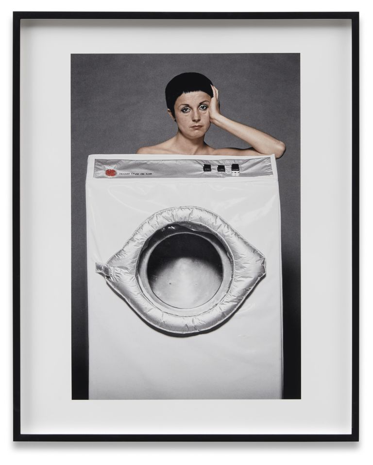 Black and white photo of a woman behind a washing machine costume, with her head visible above the machine's drum.