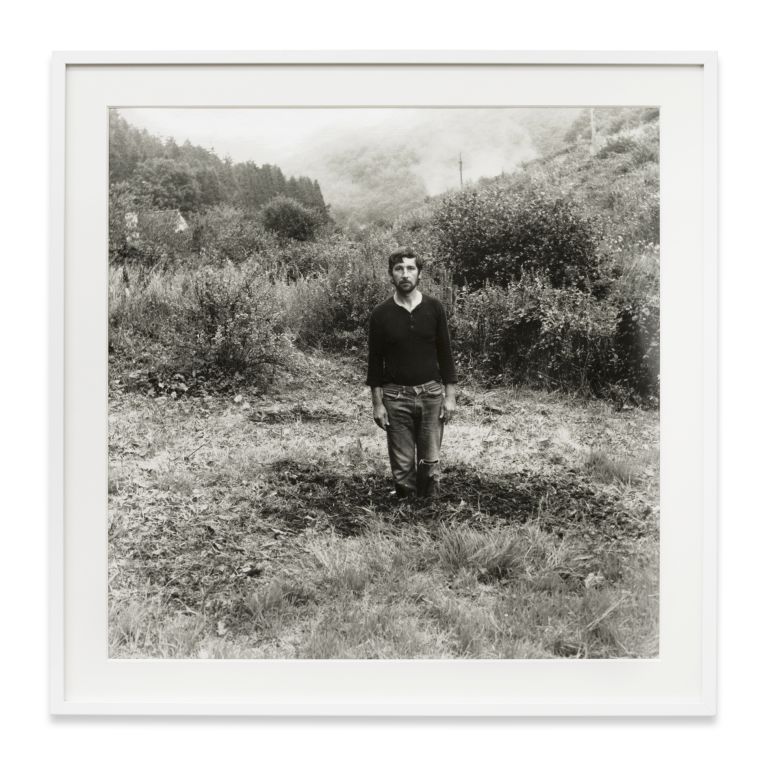 Grid of nine identical black and white photographs showing a person gradually disappearing into a landscape.