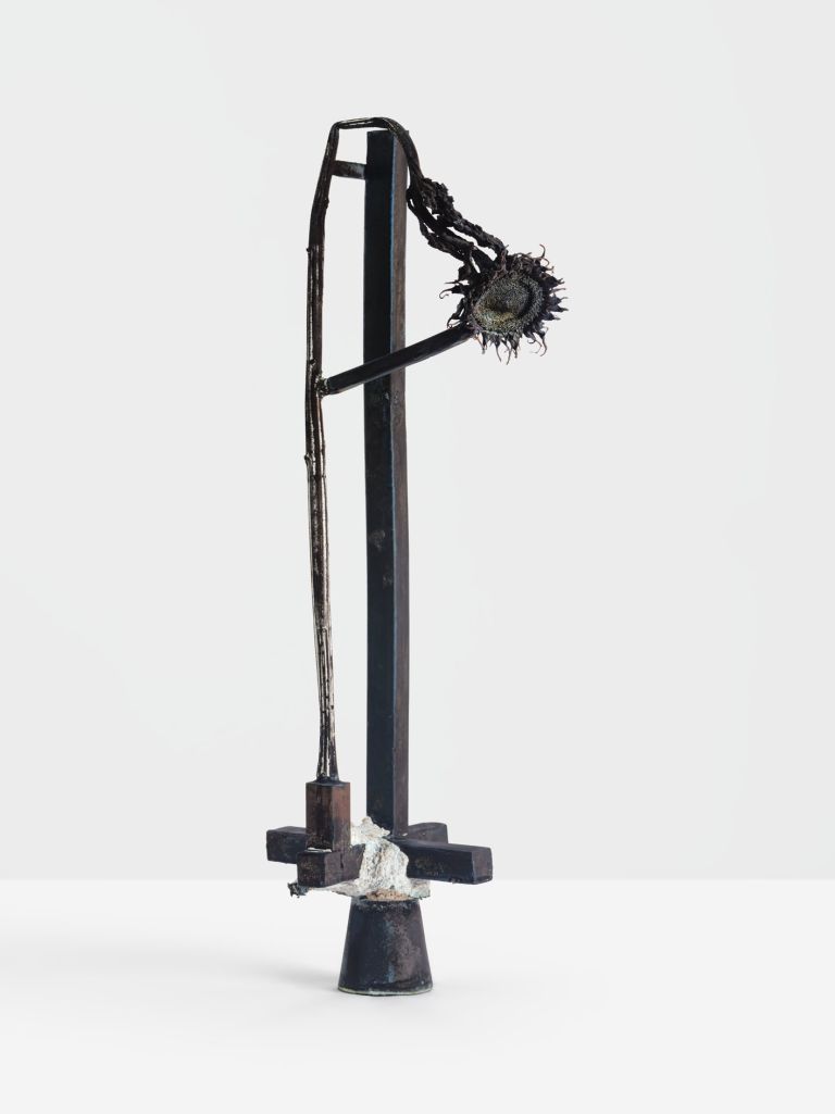 Metal sculpture with dried sunflower head attached, standing on conical base