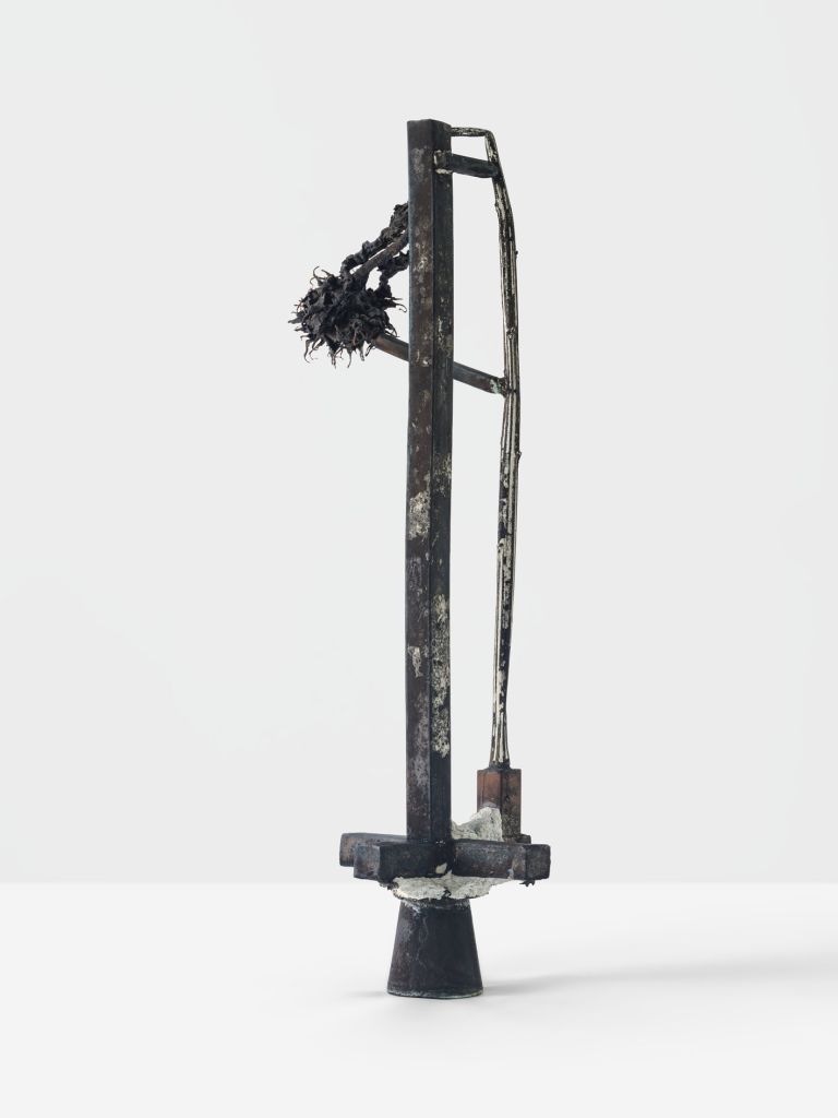 Metal sculpture with dried sunflower head attached, standing on conical base