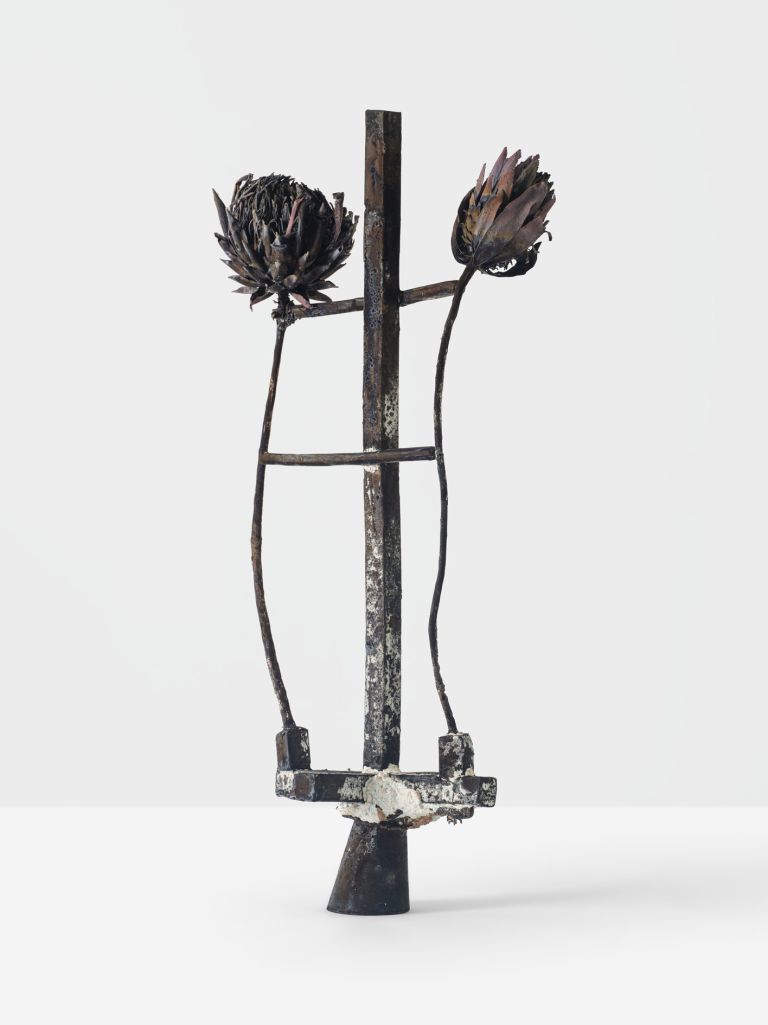 Metal sculpture with two dried artichoke heads on crossbar, standing on conical base