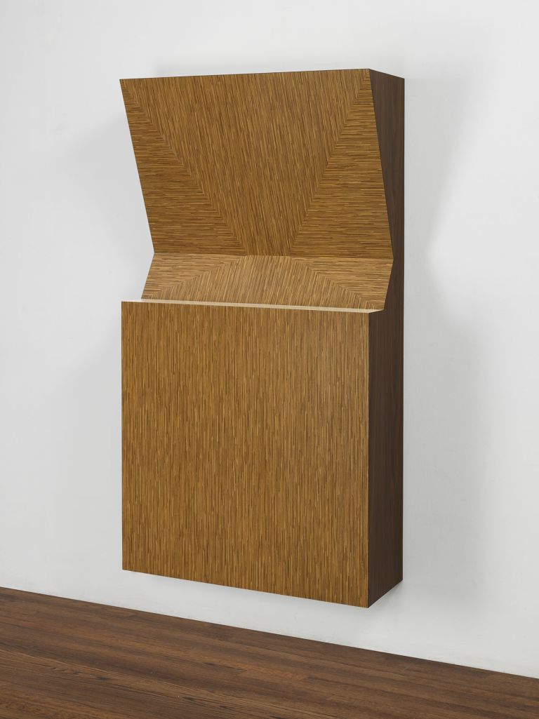 Wall-mounted warm wood relief sculpture with an upper section folded open at an angle, revealing inner grain.