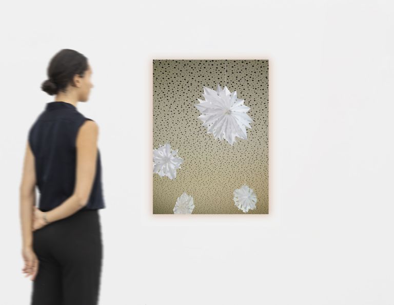 Photograph of white paper star ornaments hanging against spotted beige ceiling, varying sizes.