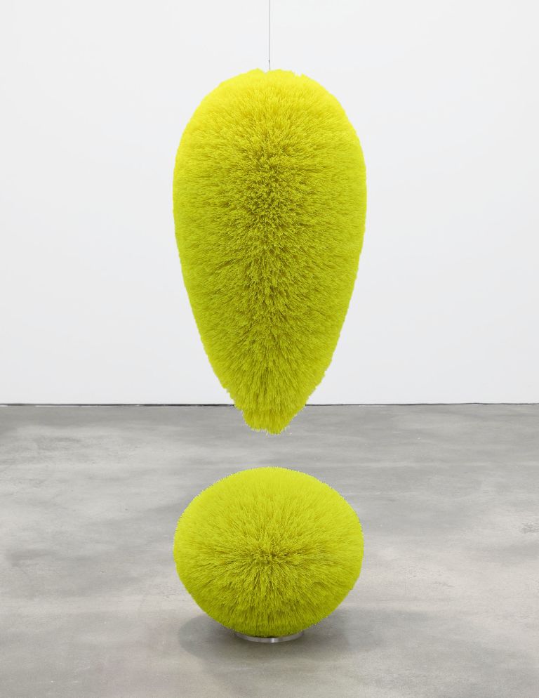Bright yellow-green fuzzy sculpture in form of exclamation mark - teardrop shape suspended above sphere on gallery floor