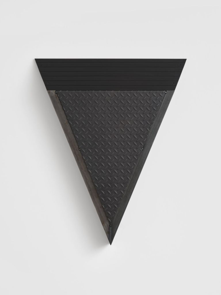 Black metal wall sculpture in downward-pointing triangle form, combining ribbed upper panel and diamond-plate textured lower surface.
