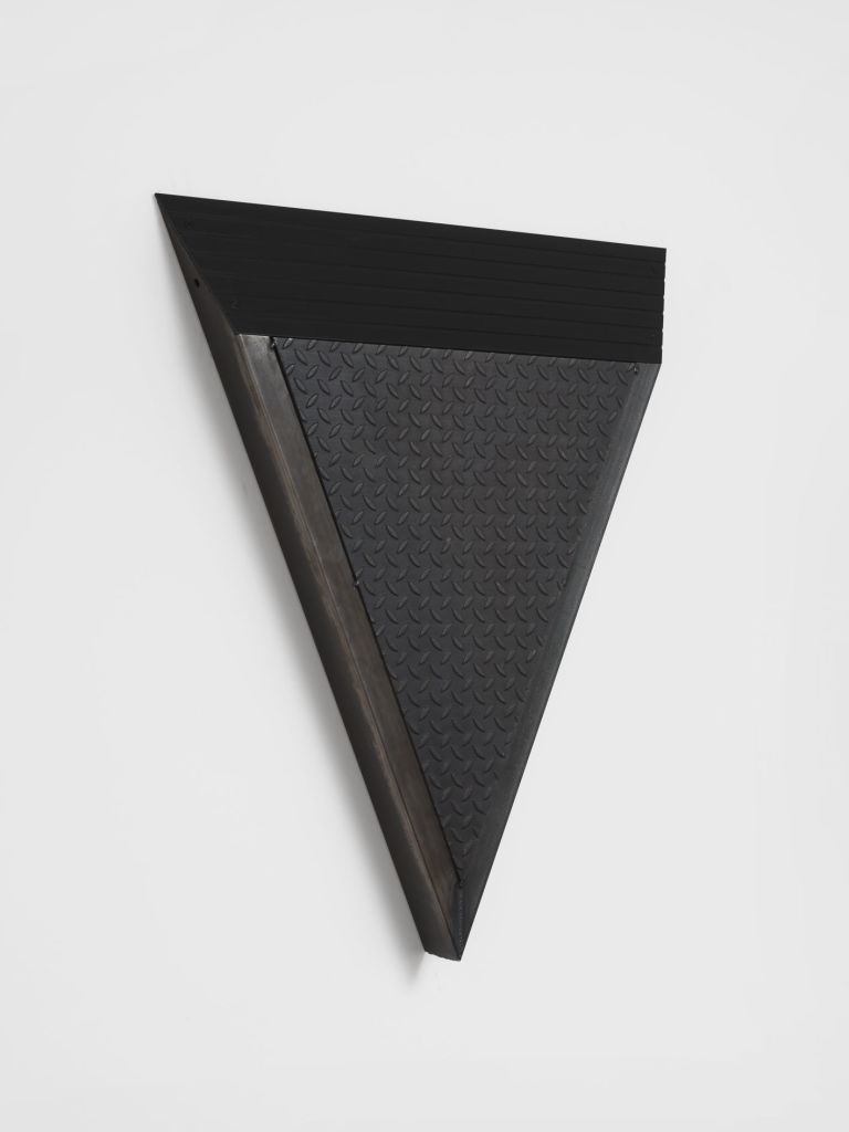 Black metal wall sculpture in downward-pointing triangle form, combining ribbed upper panel and diamond-plate textured lower surface.