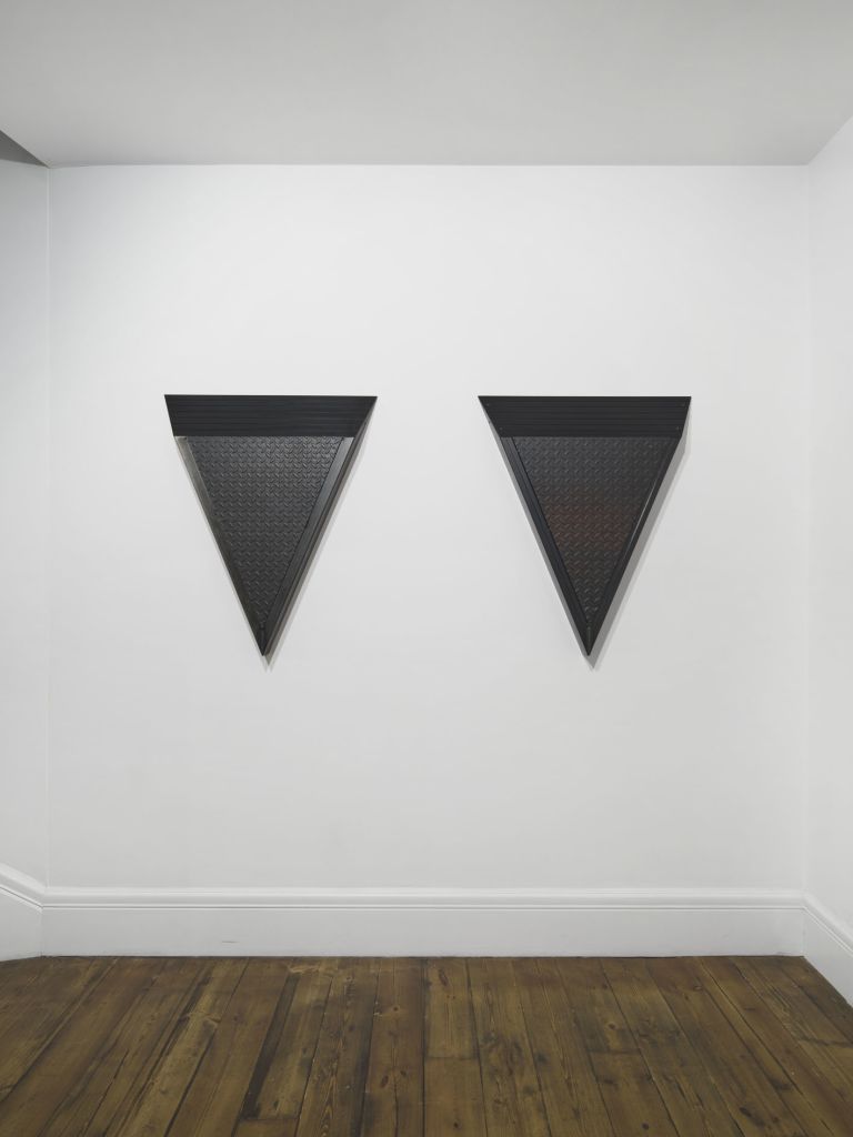 Black metal wall sculpture in downward-pointing triangle form, combining ribbed upper panel and diamond-plate textured lower surface.