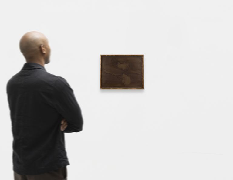 Dark abstract artwork in gold frame, featuring muted brown tones with shadowy forms and minimal detail.