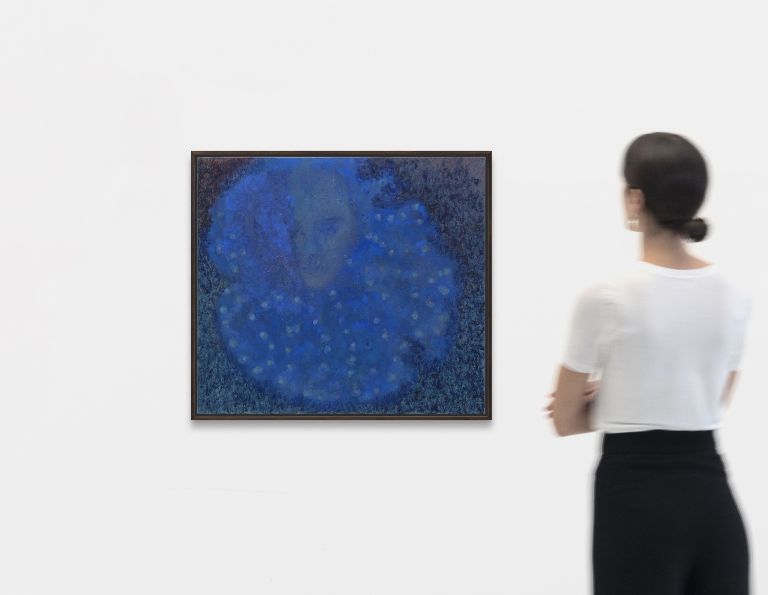 Blue painting with ethereal, cloudy forms and subtle face-like impressions emerging from deep blue and darker tones, displayed in brown frame.