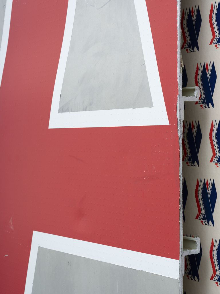 Close-up of a wall covered in repeating blue and red pattern wallpaper with a large red letter "A" mounted on an aluminum backing
