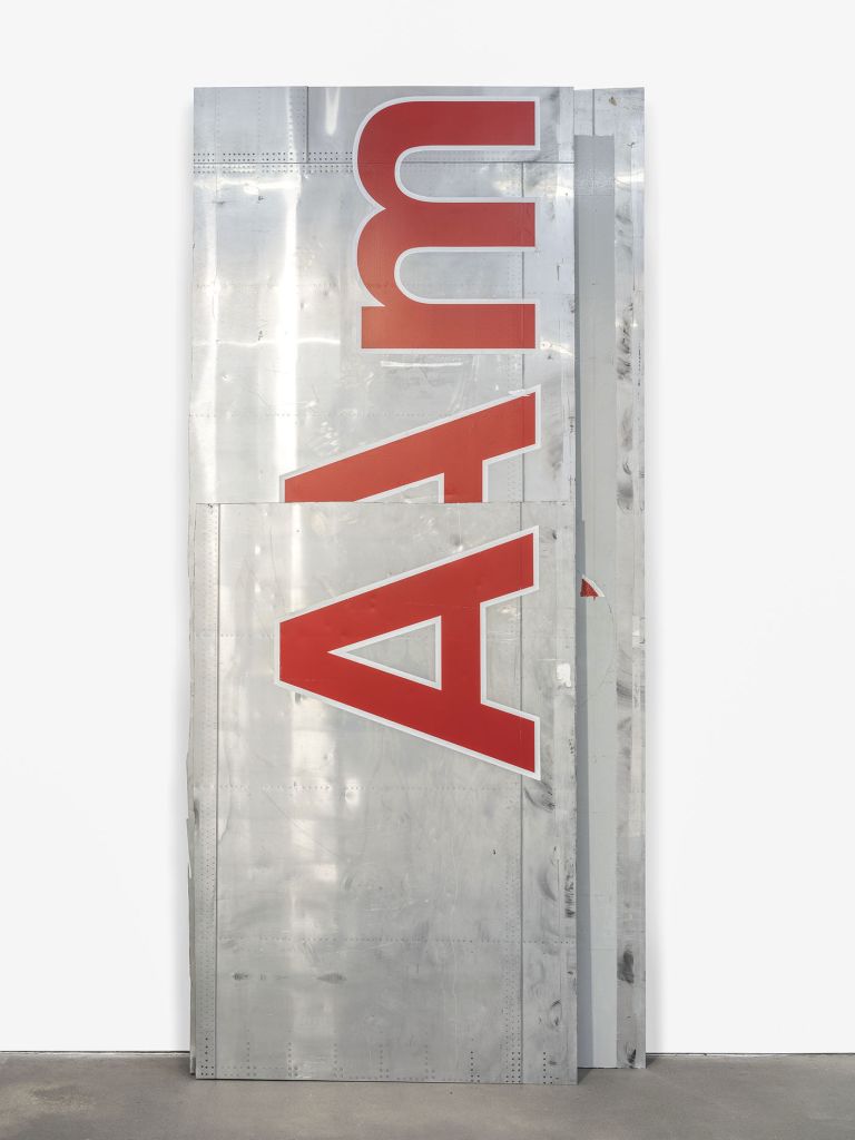 Tall metallic panel with "A Am" in large red letters mounted vertically on a reflective silver surface with visible rivets
