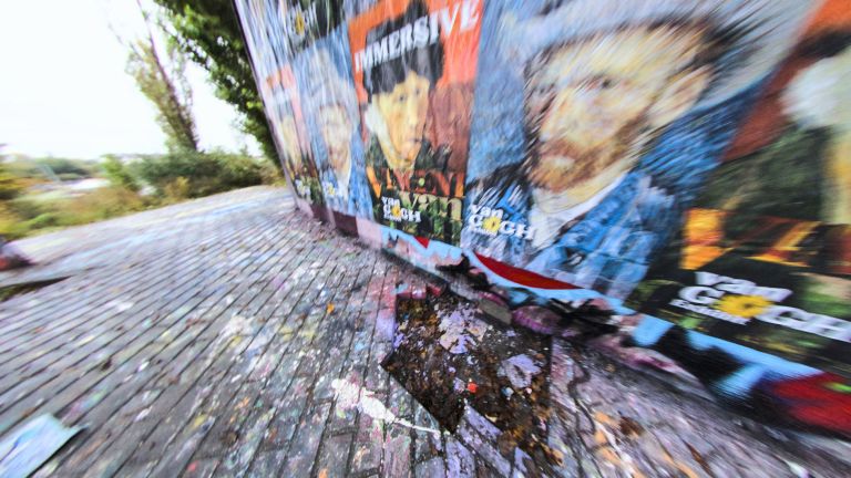 Motion-blurred view of colorful street art and graffiti on a wall beside cobblestone pavement, creating a dynamic spinning effect.