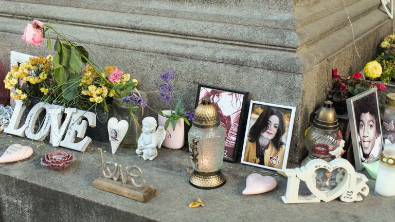 Memorial display on stone steps with flowers, candles, photographs, and "LOVE" letters creating a tribute arrangement.