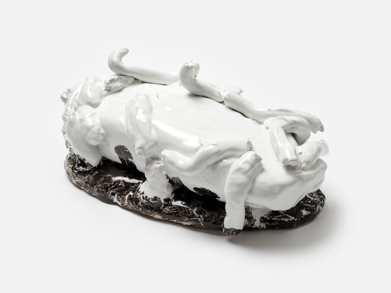 A black and white sculptural ceramic object with protruding elements resembling bones or limbs, partially resting on a black base, photographed against a white background.