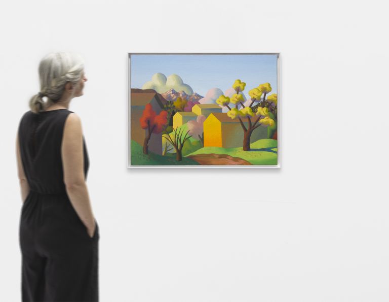 Colorful landscape painting with stylized trees in autumn colors, geometric yellow and pink houses, mountains, and fluffy clouds against a blue sky