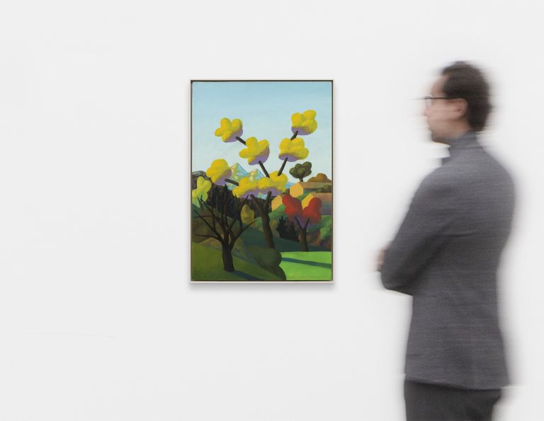 Whimsical landscape painting with yellow autumn trees, mountains, small geometric houses, and rolling green hills under a pale blue sky