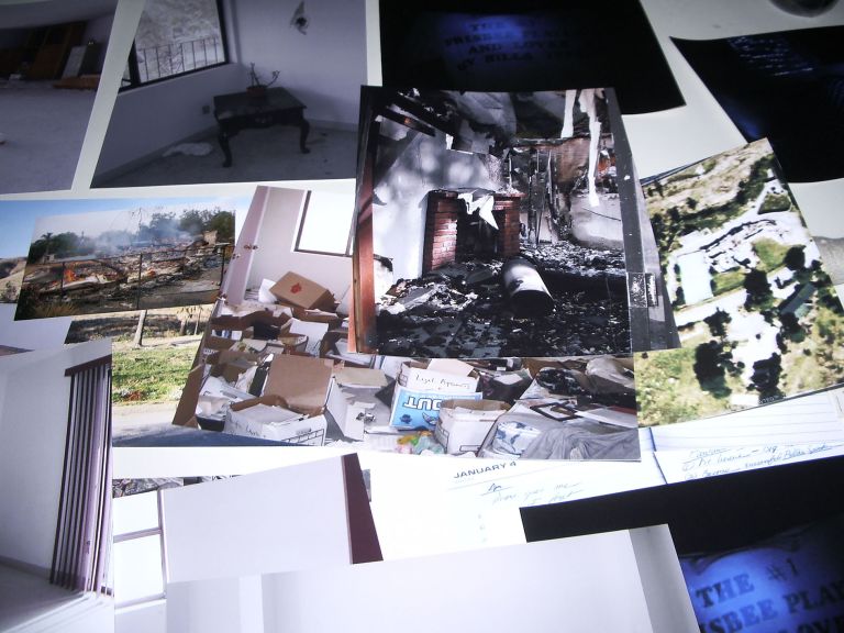 Collection of printed photographs showing damaged rooms, debris, and destruction spread across a dark surface