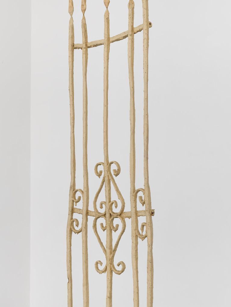 Tall vertical sculptural installation with geometric patterns mounted on white gallery wall.