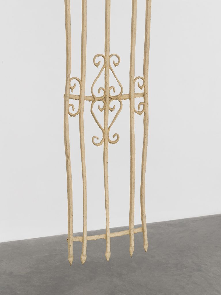 Tall vertical sculptural installation with geometric patterns mounted on white gallery wall.