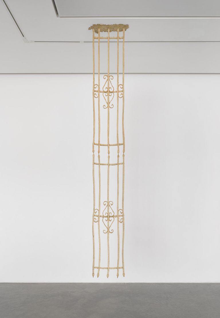 Tall vertical sculptural installation with geometric patterns mounted on white gallery wall.
