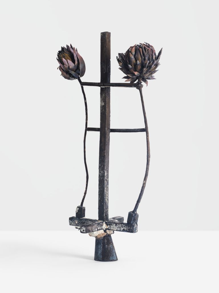 Metal sculpture with two dried artichoke heads on crossbar, standing on conical base