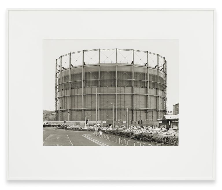 Black and white photograph of a massive gas storage tank with detailed metal framework and support structure