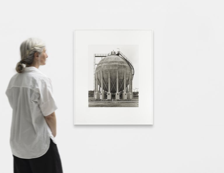 Black and white photograph of a massive gas storage tank with detailed metal framework and support structure