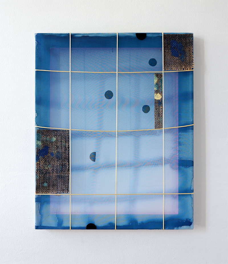 A rectangular abstract artwork with a translucent grid stretched over a frame. The composition features layered shades of blue with hints of purple, scattered black circular shapes, and two textured fabric patches with dark woven surfaces on the left and upper right.