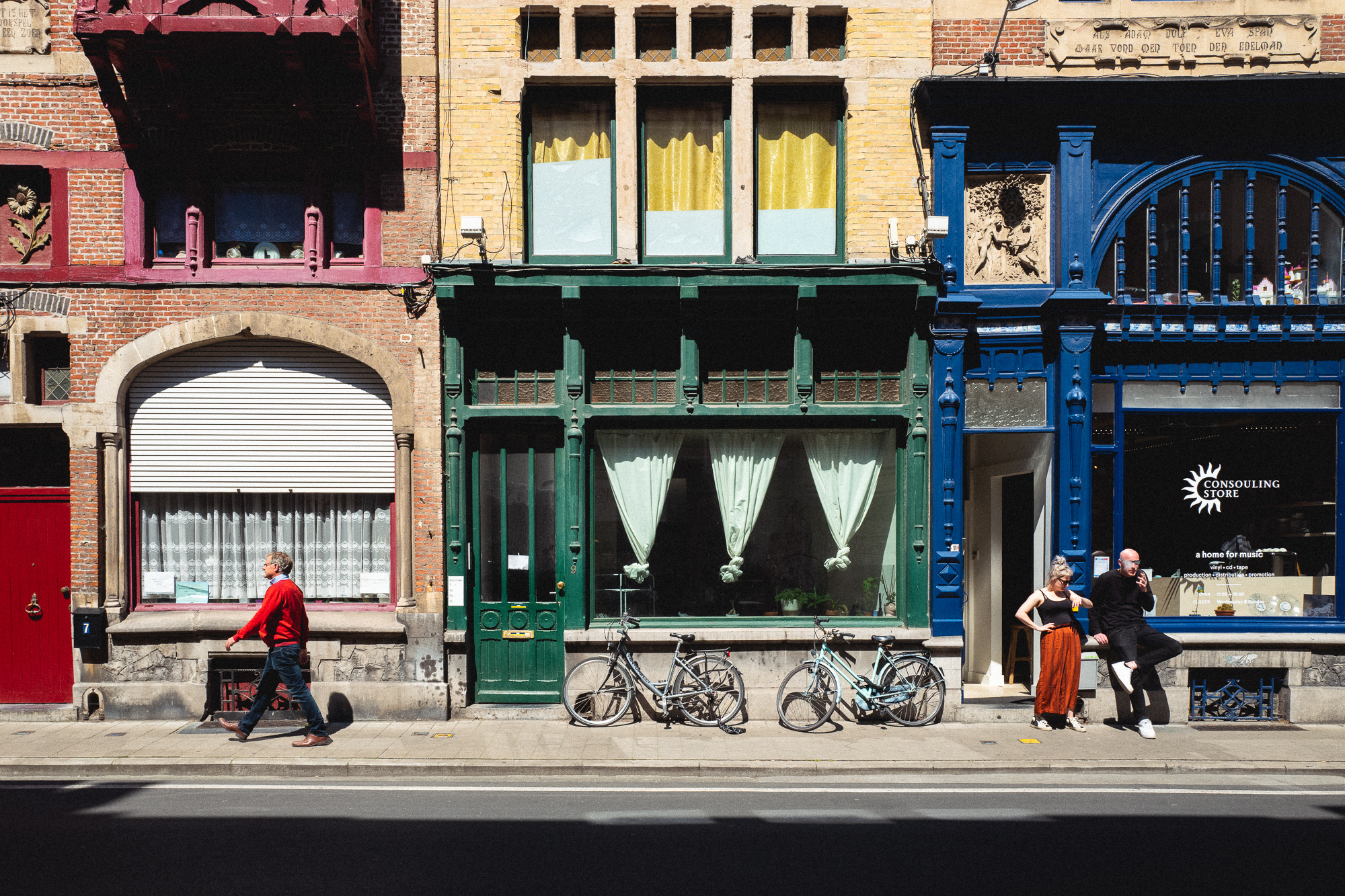 A couple stand outside a record store while a man continues on his way down the sidewalk.