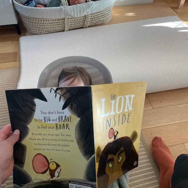 Child reads the picture book “The Lion Inside” while seated in a baby rocker.