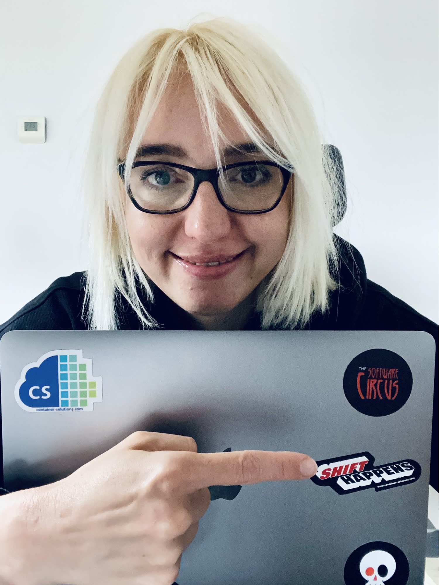 Sevi Karakula atrás de um laptop, estendendo o braço e apontando para um adesivo da Container Solutions que diz "Shift happens"