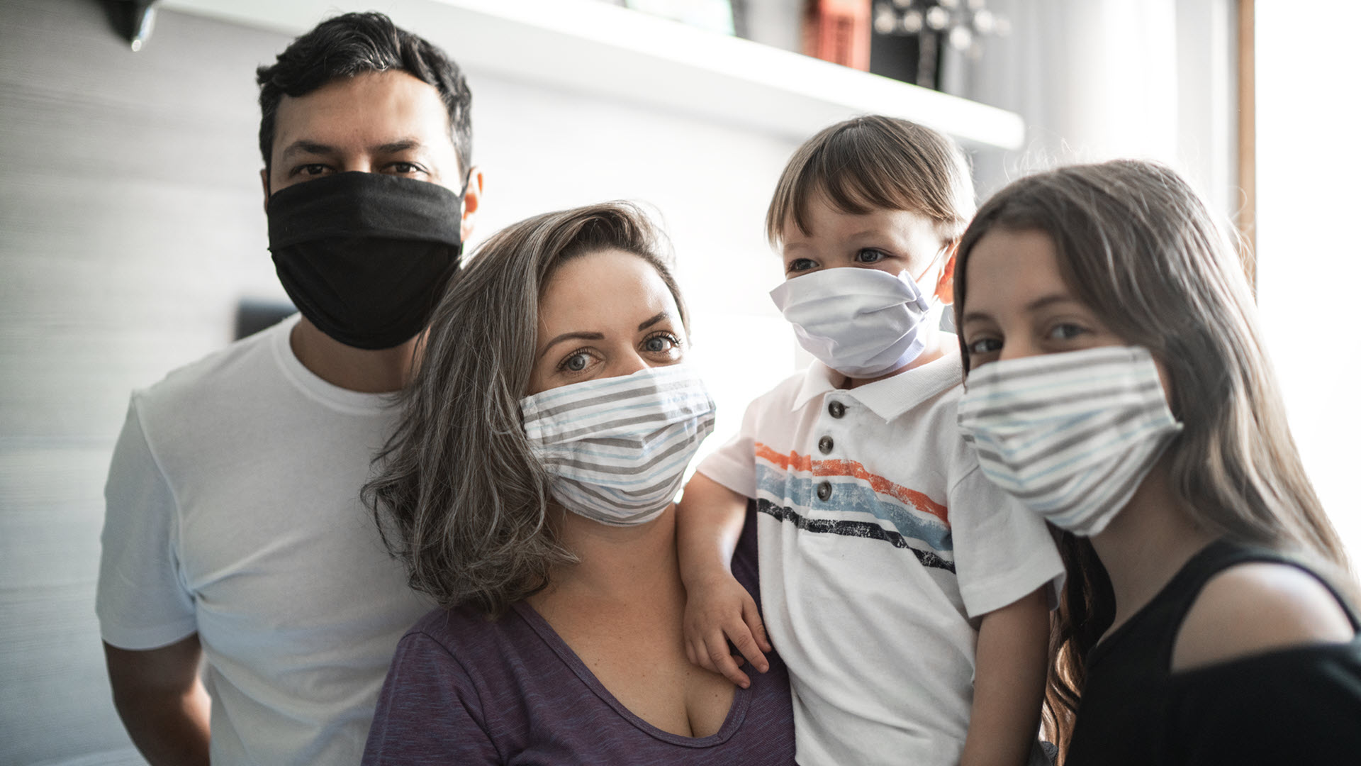 Family of four wearing masks staring attentively at the camera