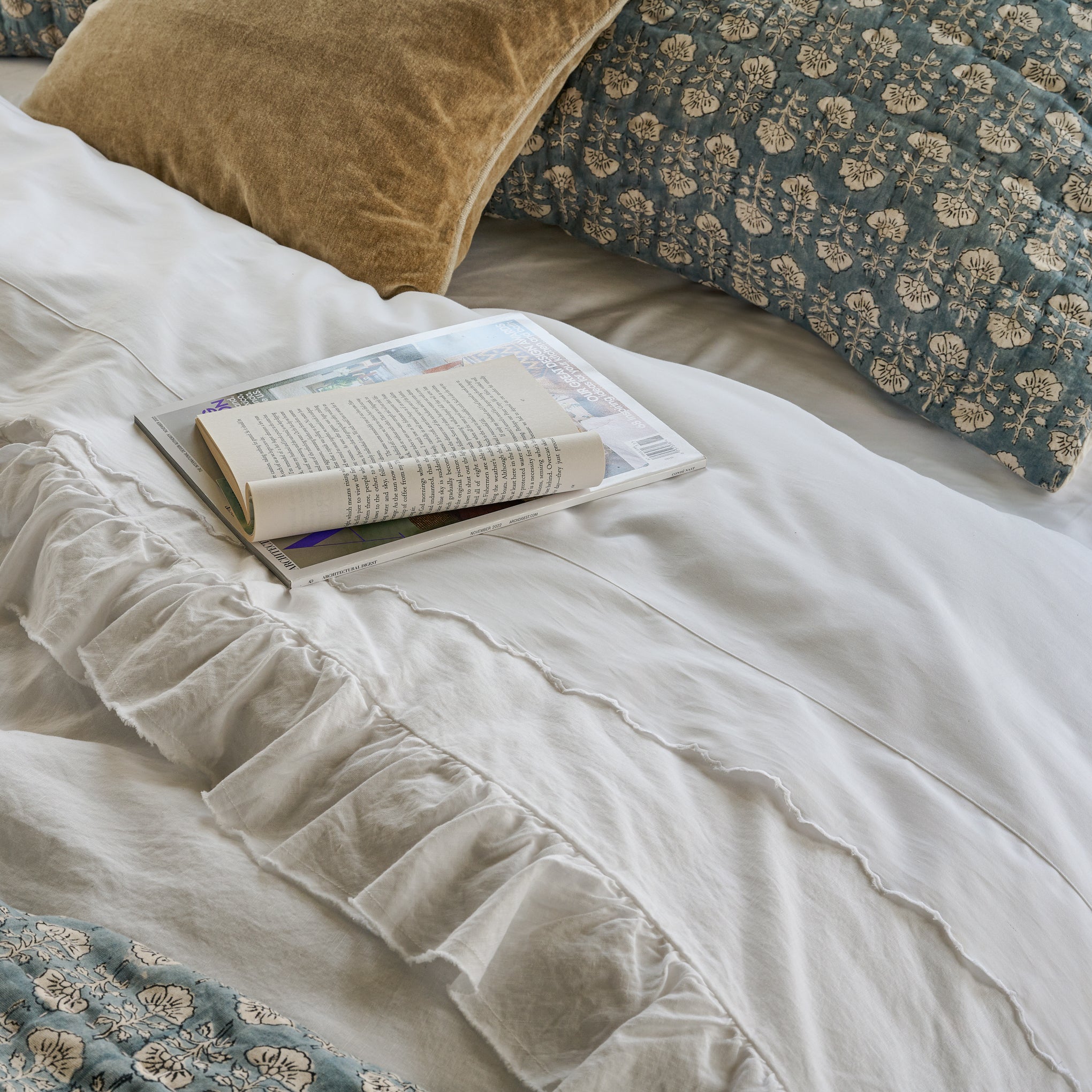 Bed layered with blue floral quilt and Optic White Ruffle Duvet Cover Items range from $180.00 to $200.00