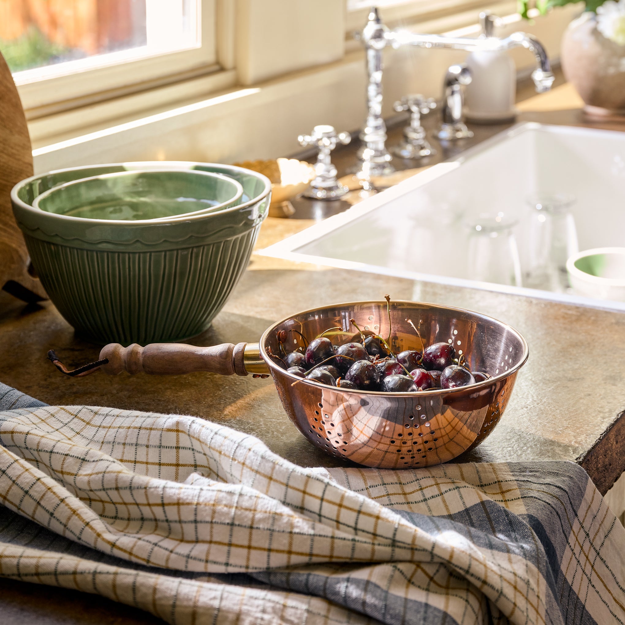 Copper Colander with Walnut Handle containing cherries on a countertop next to a tea towel