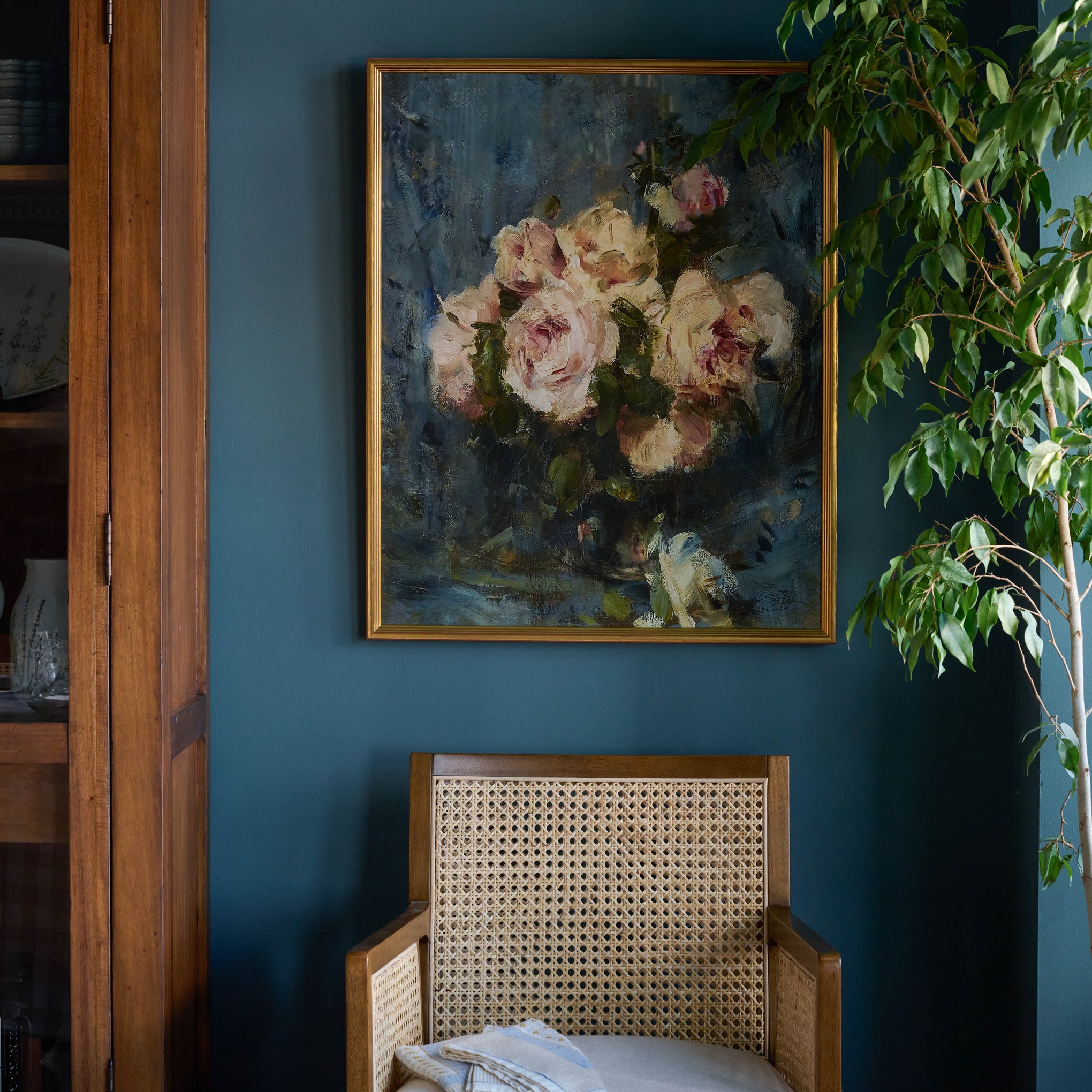 Still Life with Roses in a Glass Vase hanging on a blue wall above a chair