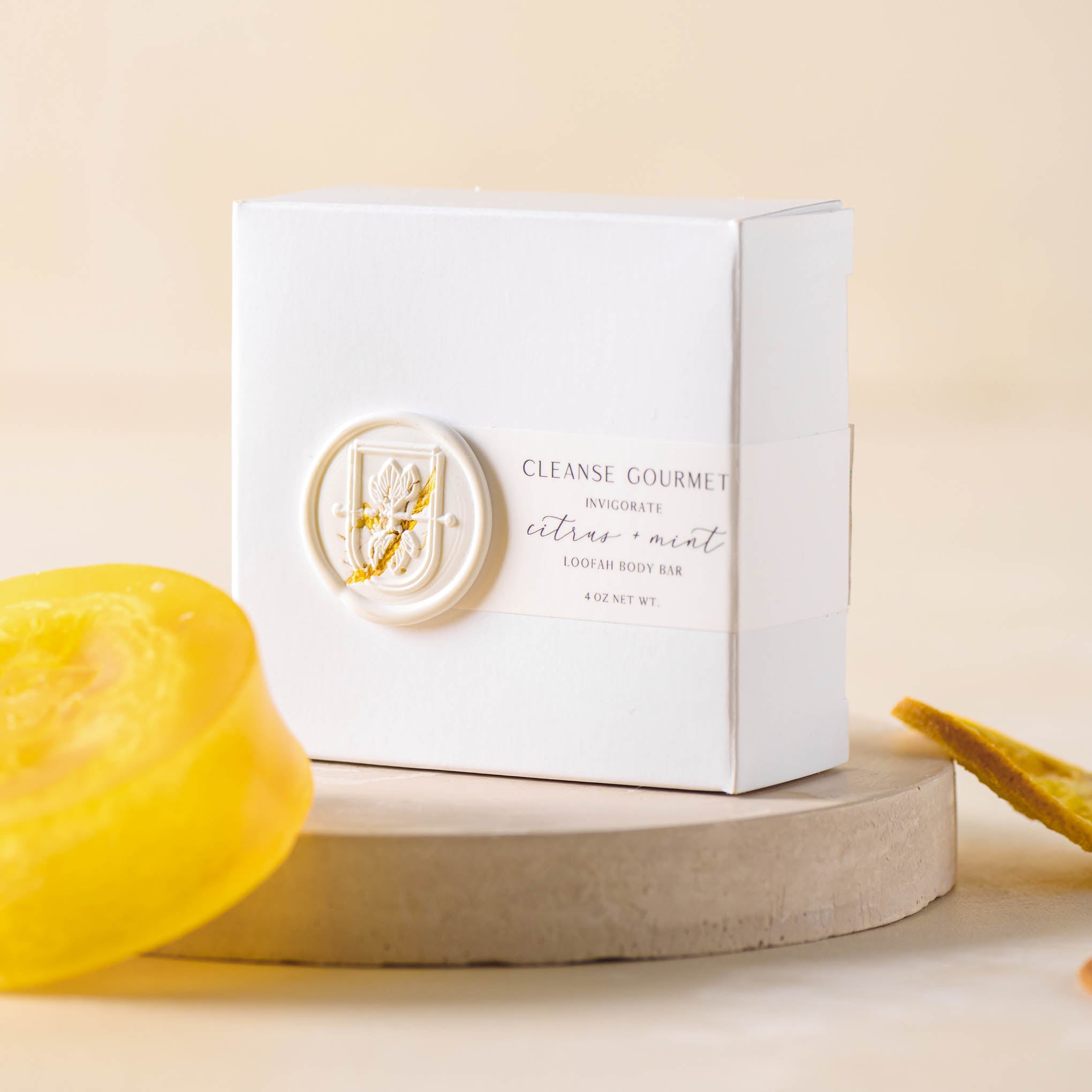 Yellow circular bar of soap next to box that reads Cleanse Gourmet invigorate citrus and mint loofah body bar 4 oz. net wt. On sale for $11.20, discounted from $14.00