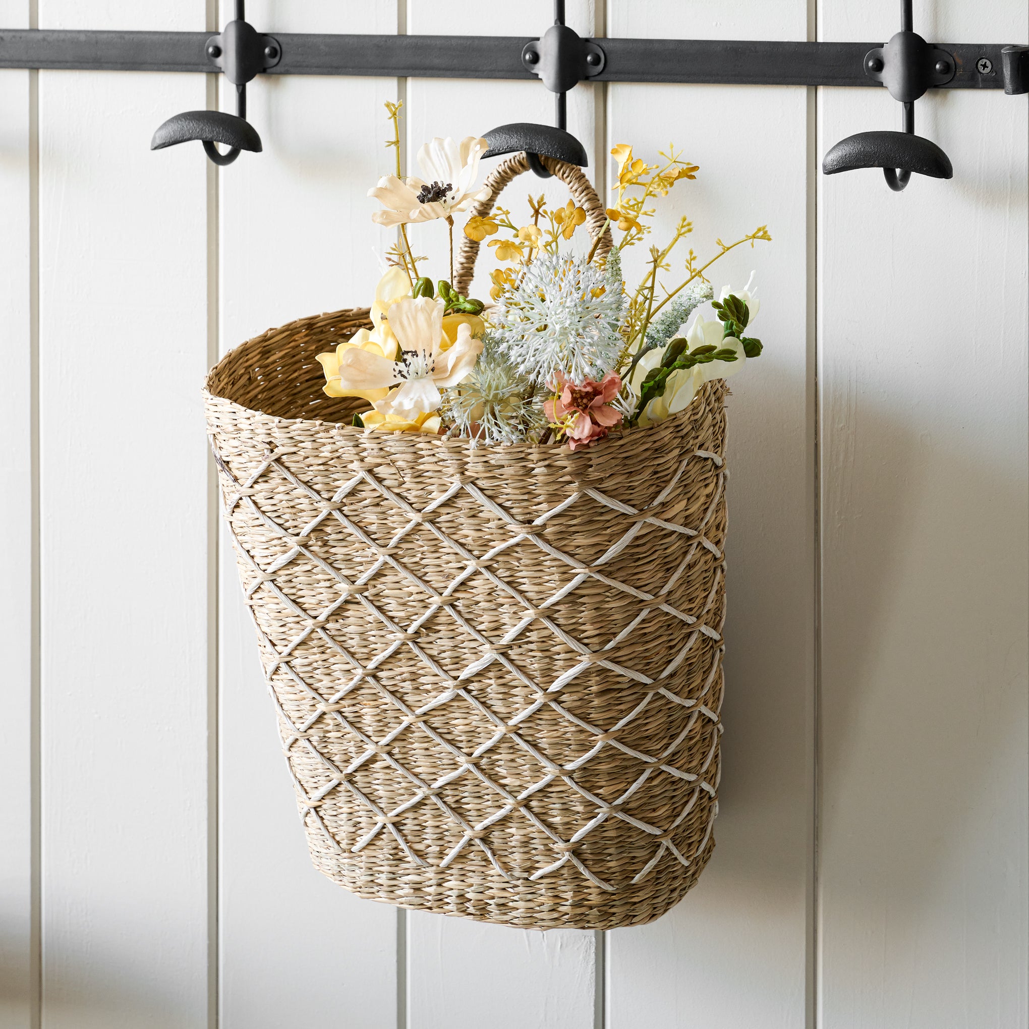 Close up of Cecily Hand-Woven Wall Basket on hook containing flowers in basket