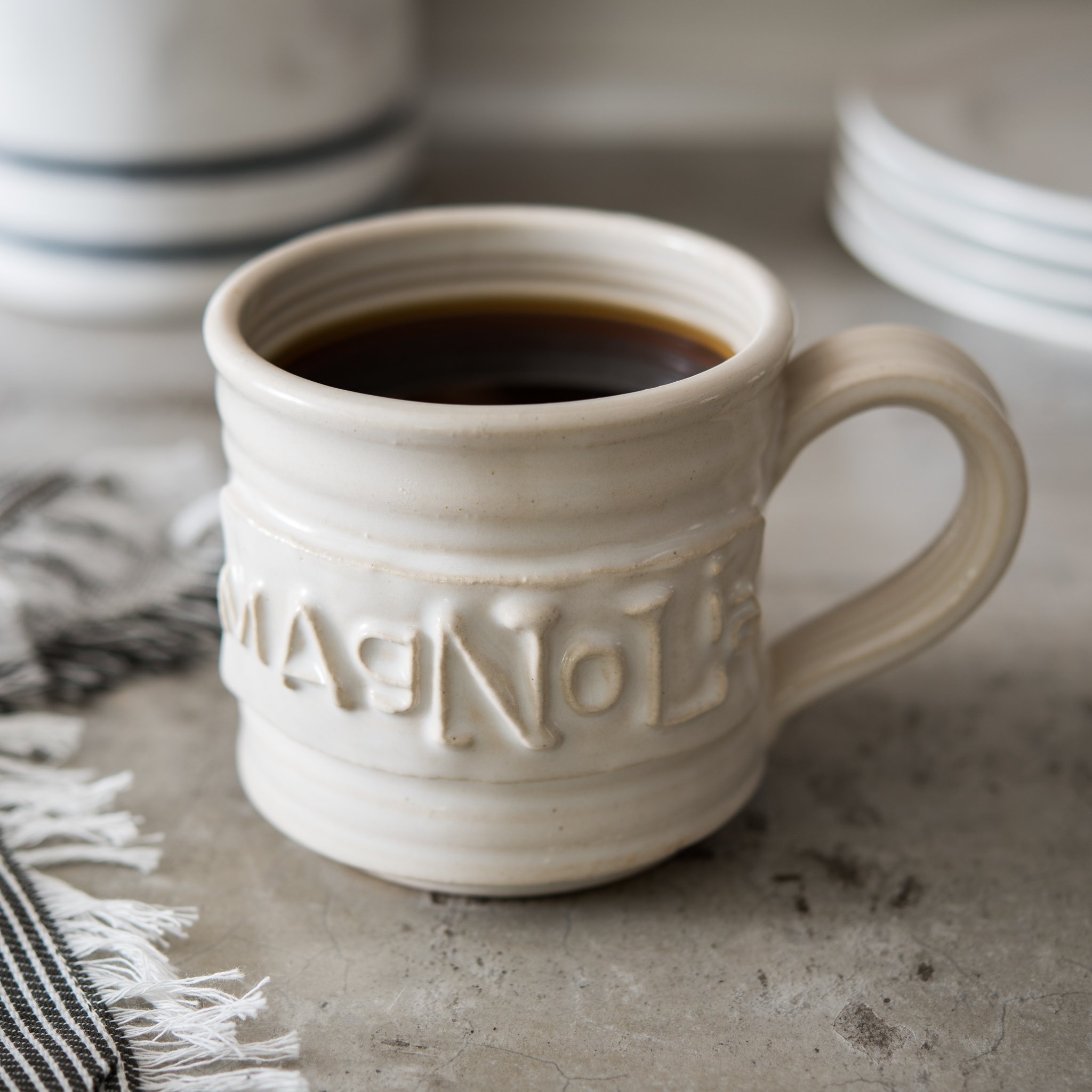 white handthrown ceramic mug with original Magnolia logo embossed on side $24.00