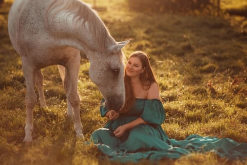 /_vercel/image?url=/Girl+in+long+dress+sitting+on+the+grass+with+her+horse+during+summer+sunset.&w=1536&q=100