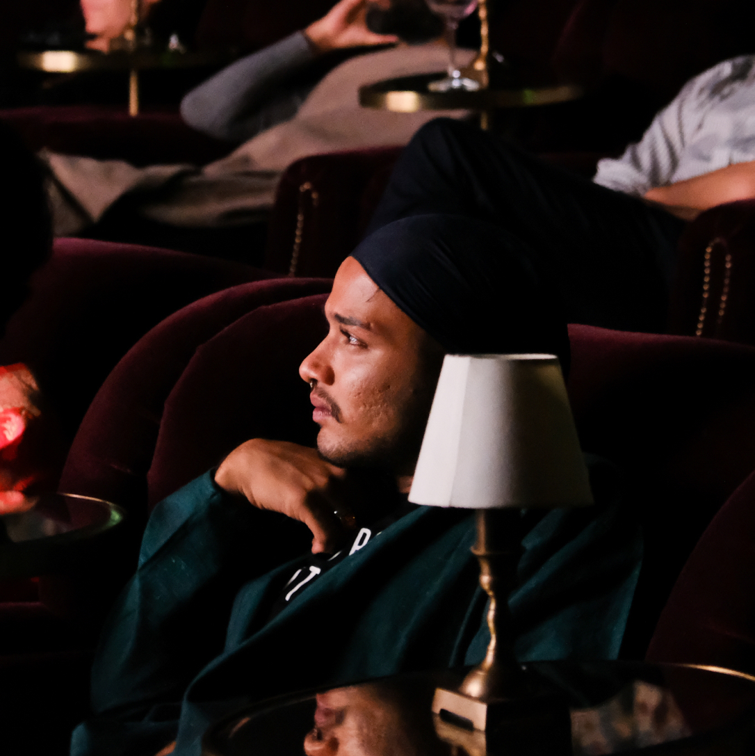 A man sitting in a row of cinema chairs with other people watching something.