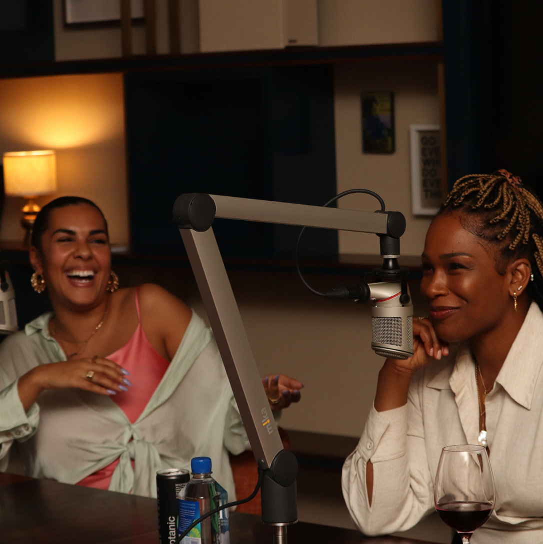 Two women using recording equipment in an office with one laughing at the other.